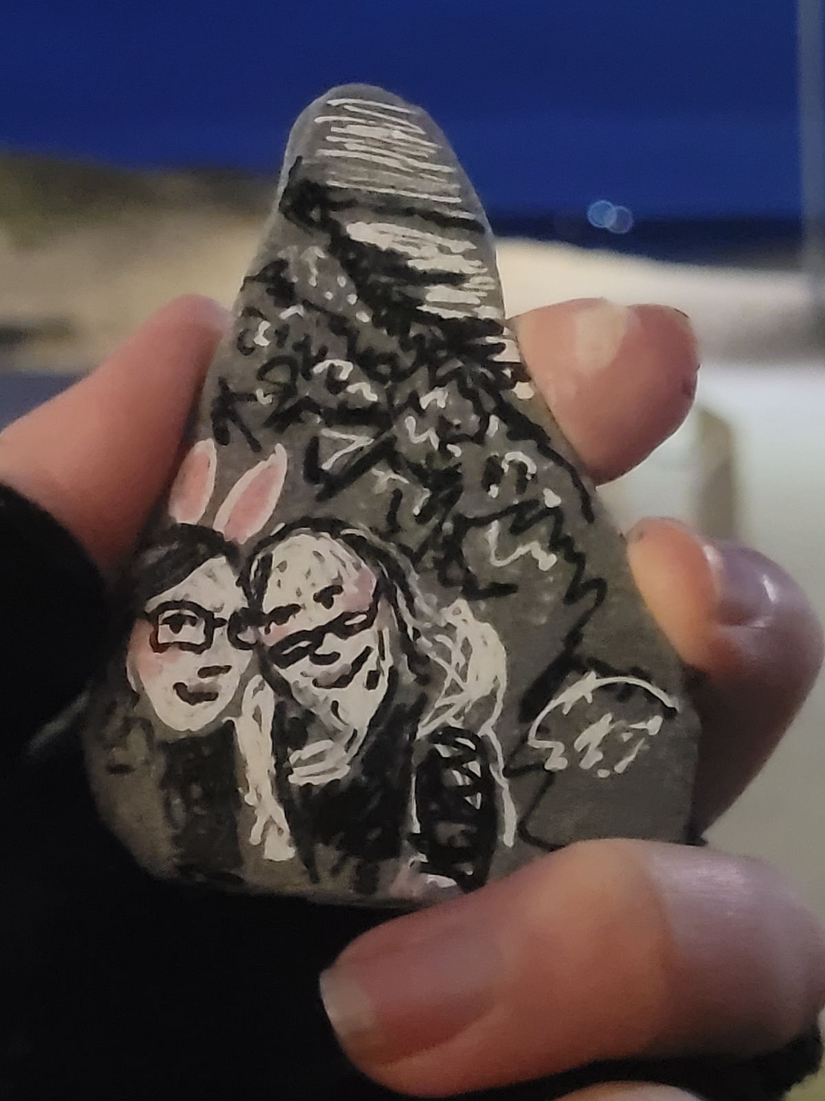 You Rock. Photograph of a rock on which an image of the artist and their partner is painted. The artist is wearing white and pink bunny ears.